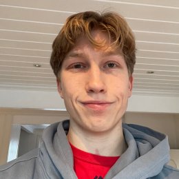 Ung mann med blondt hår og grå hettegenser smiler forsiktig mot kameraet.