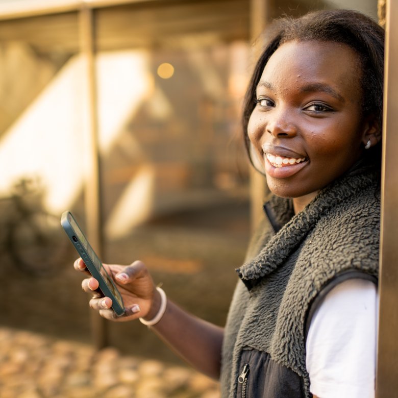 Ung kvinne smiler og holder en mobiltelefon utendørs.