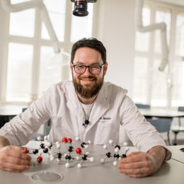 Mann i labfrakk holder molekylmodell i et moderne laboratorium.