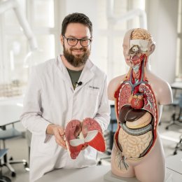 Mann i hvit frakk viser anatomisk modell og holder modell av lunger i et klasserom.