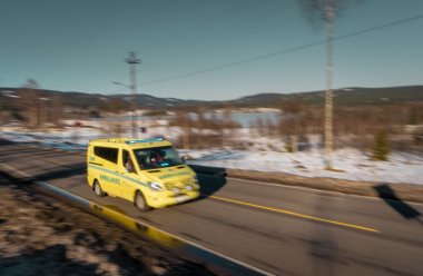 Gul ambulanse kjører raskt på en landevei i vinterlandskap.