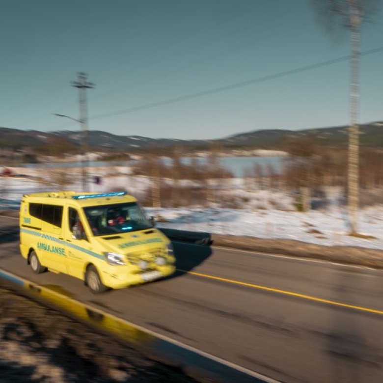 Gul ambulanse kjører raskt på en landevei i vinterlandskap.