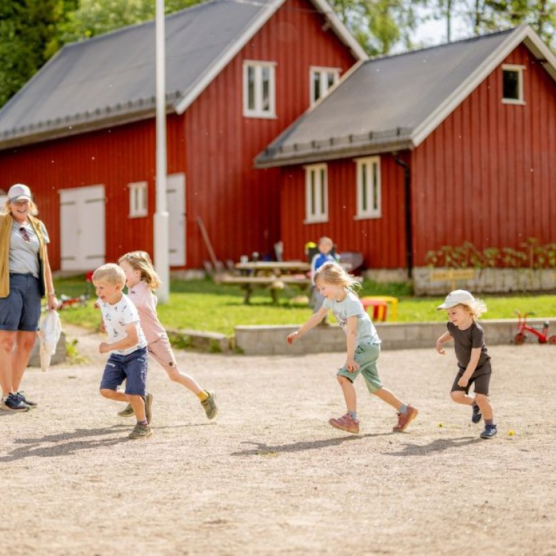 Barn leker utendørs foran en rød bygning på en solrik dag.