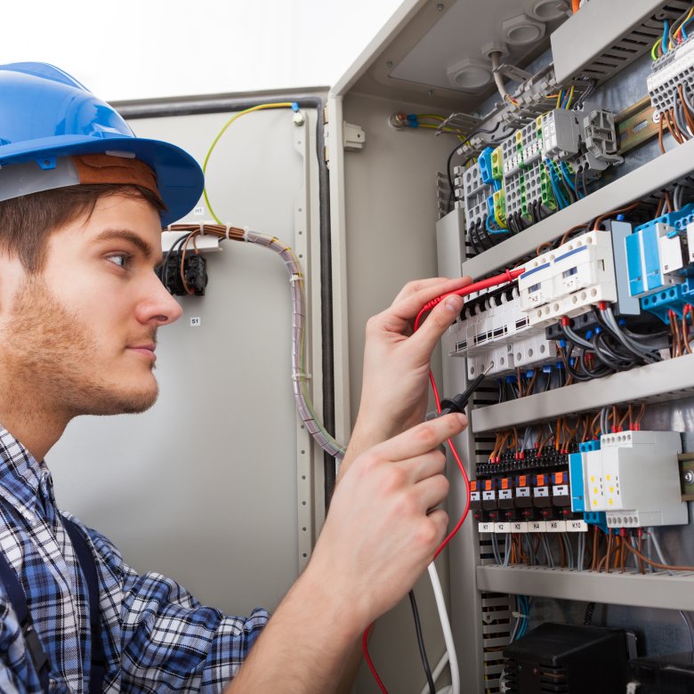 Elektriker med blå hjelm jobber med ledninger i et åpent elektrisk skap.