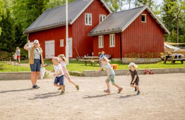 Barn leker utendørs foran en rød bygning på en solrik dag.